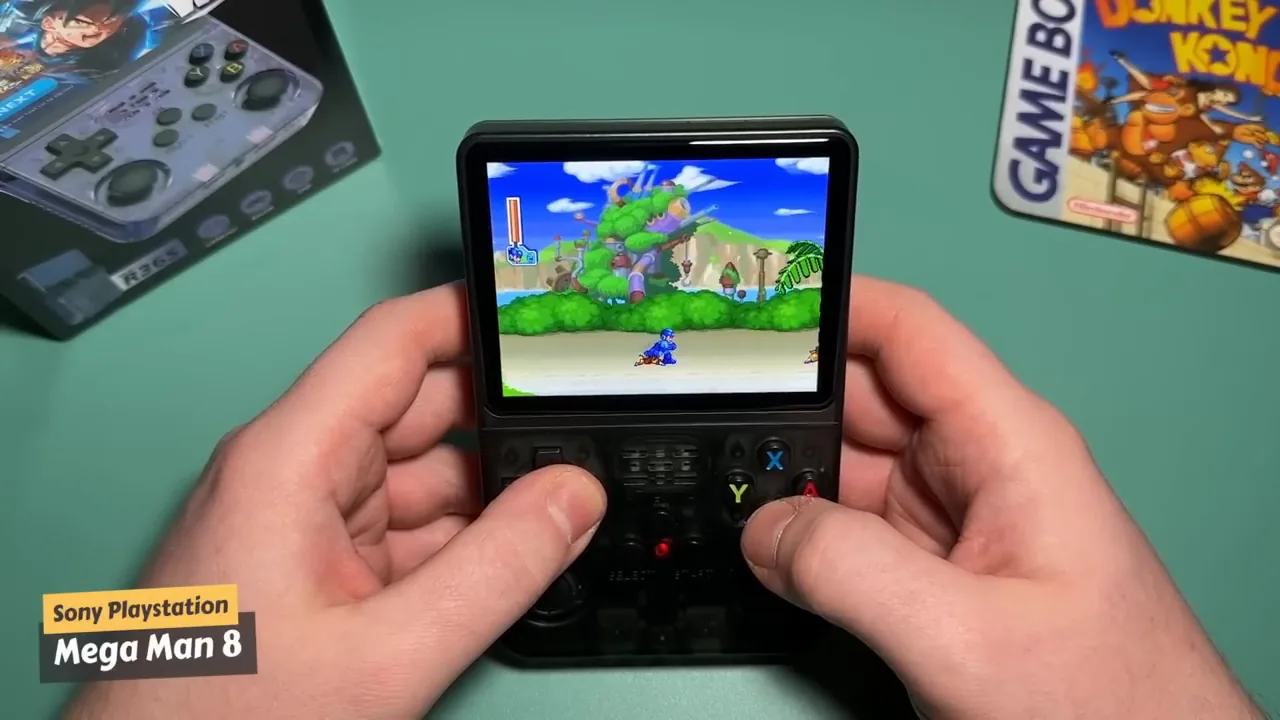Console R36S noire tenue en mains avec un jeu PlayStation à l'écran, console rétrogaming portable à 50 euros