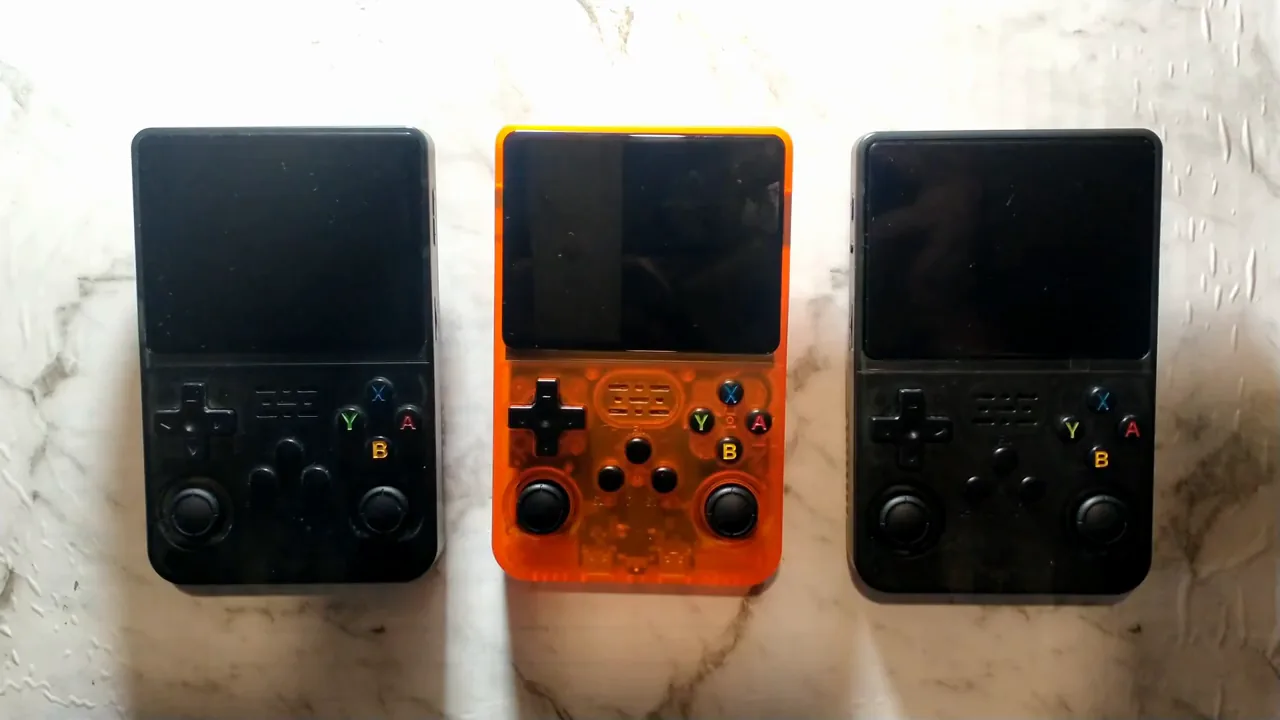 Trois consoles R36S côte à côte, noire, orange translucide et noire, pour comparer vraie, clone et fausse